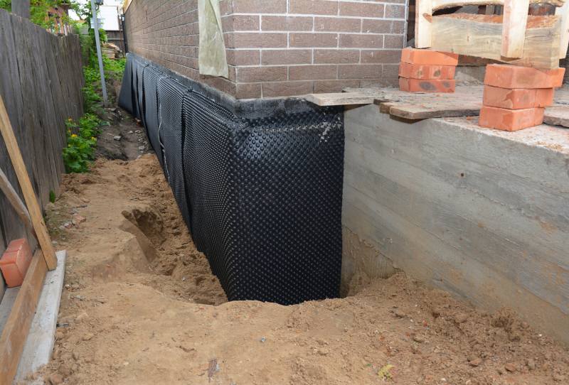 waterproofing below grade in san jose - Rscwp Excavated trench along the house foundation with a black perforated drainage membrane installed against the wall, awaiting further backfill.